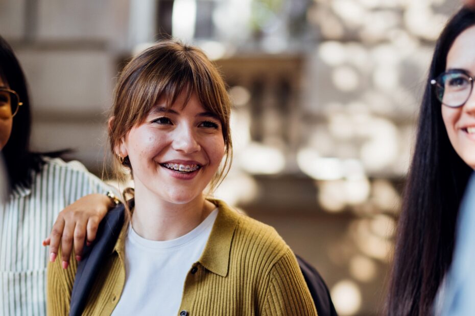 Un groupe de jeunes étudiants joyeux se rassemble dehors, discutant et riant sous un soleil radieux. Ils respirent la joie et la camaraderie, créant une atmosphère positive.
